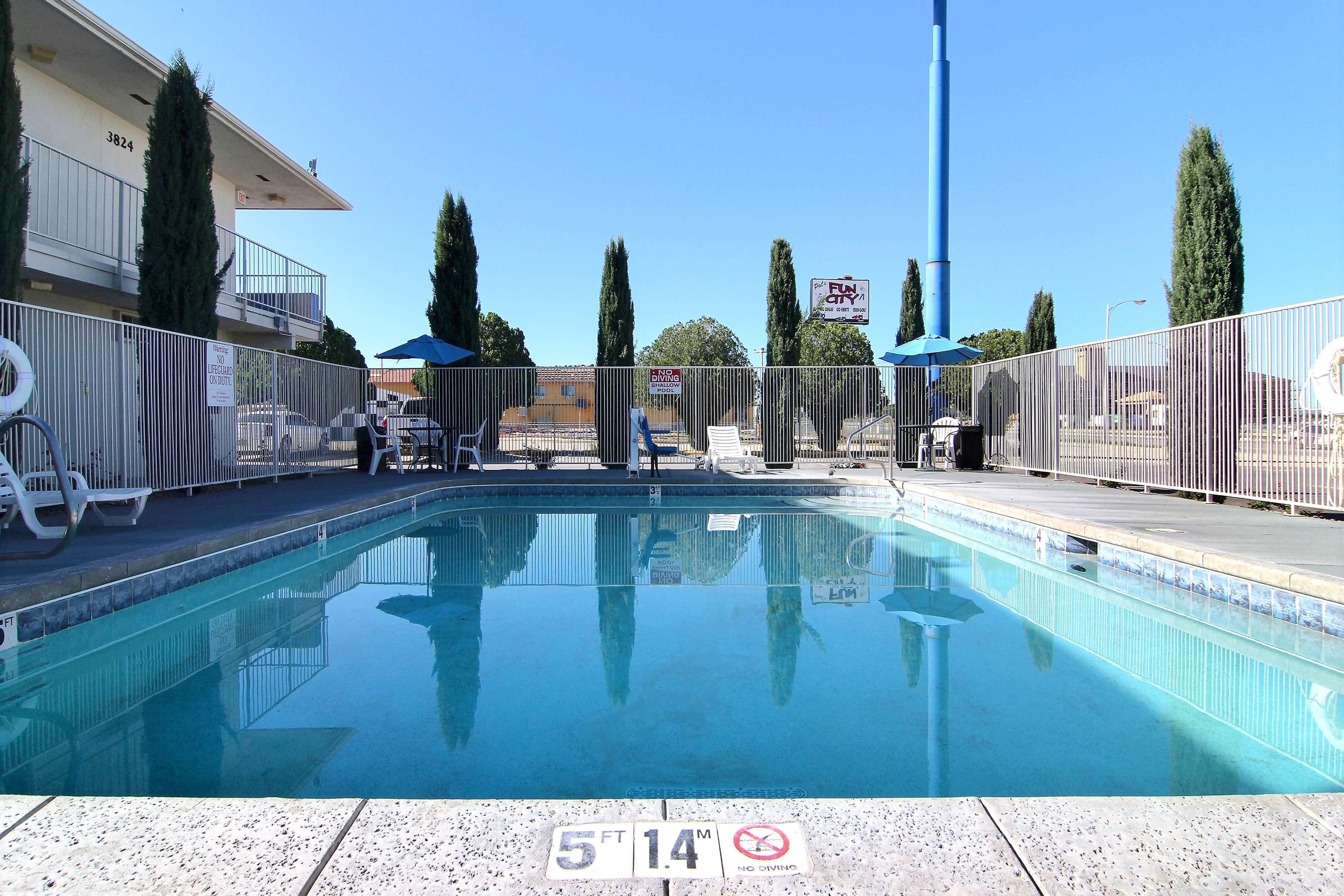 Una piscina con indicador de profundidad de 5 pies y 14 pulgadas, rodeada por un área cercada con sillas de descanso y sombrillas.