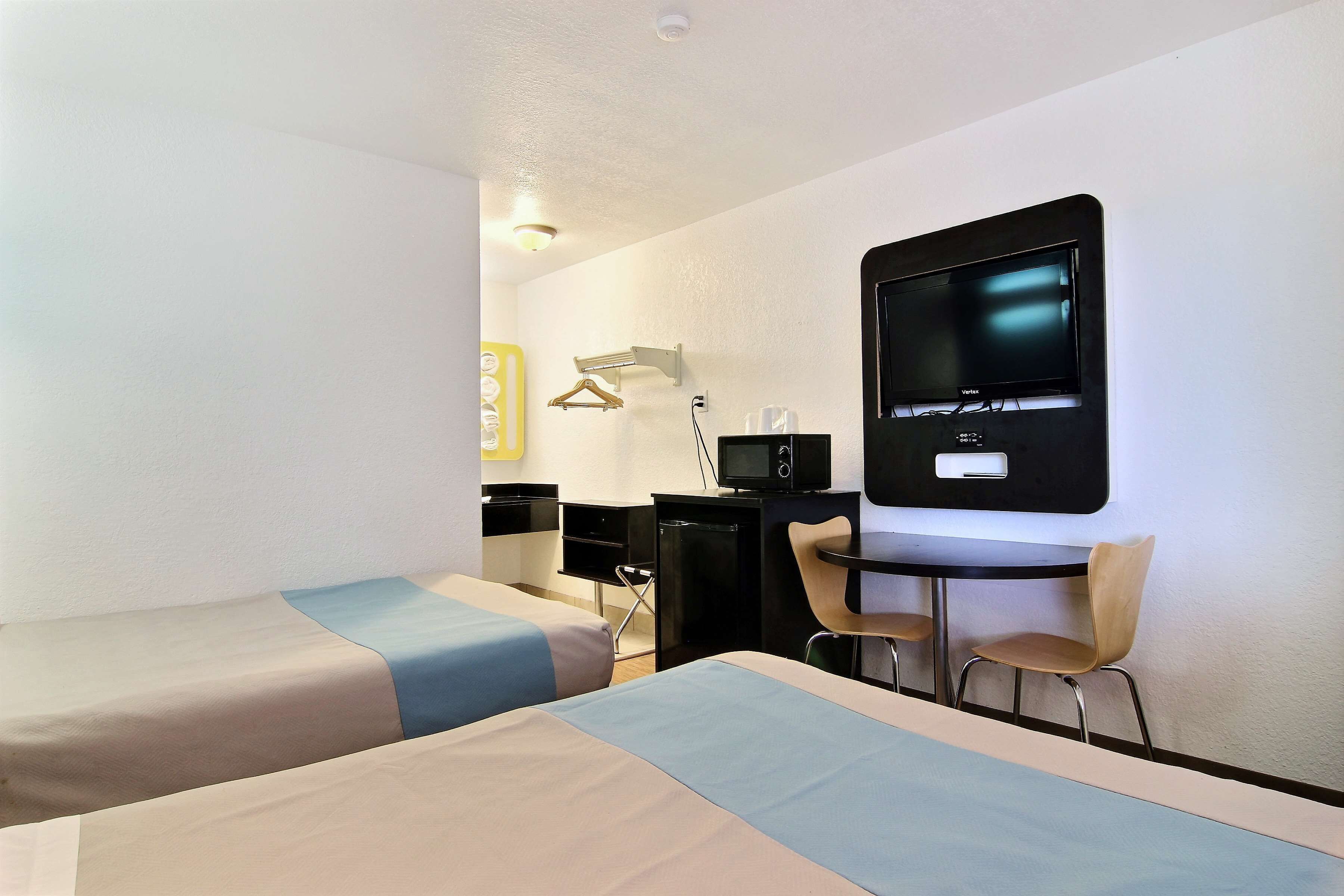 A hotel room with two beds, a desk with a computer, a TV, and two chairs.