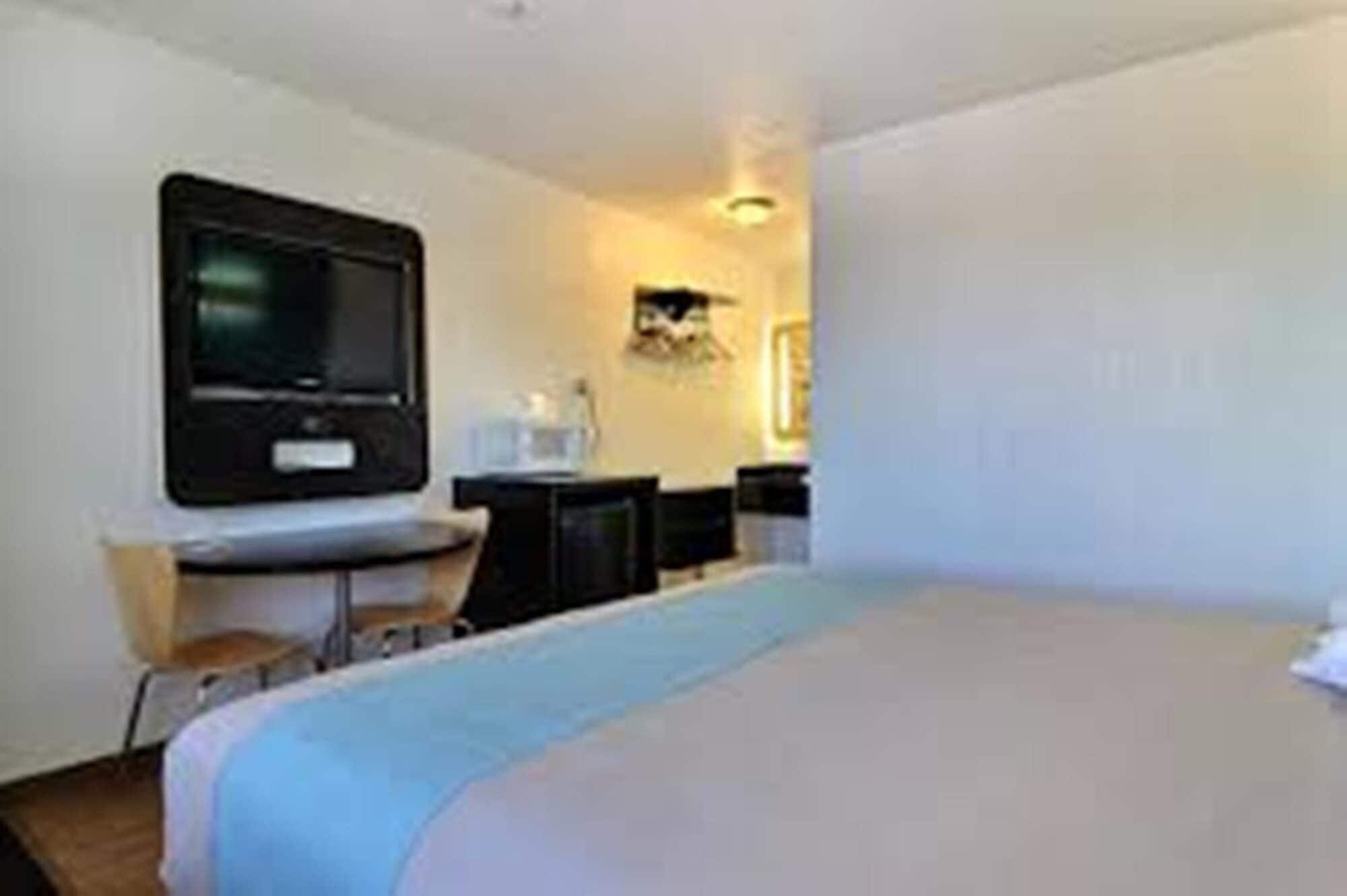 A hotel room with a bed, a desk, a chair, and a television.