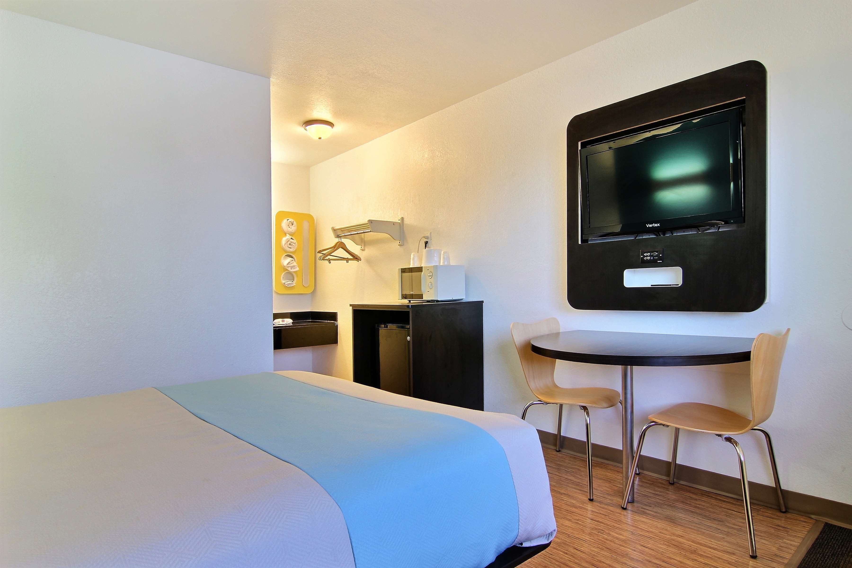 A hotel room with a bed, a desk, a chair, a TV, and a small kitchenette.