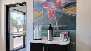 Ein Empfangsbereich mit Glastür, die nach draußen führt, einem Poster mit einer Straße, dem Schriftzug 'GOIN' 6' und dem Text 'Nationalparks', einer Wasserflasche und einer Kaffeemaschine auf einer Theke.