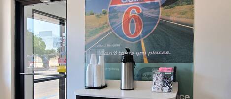 A reception area with a glass door leading outside, a poster of a road with 'GOIN' 6' and 'national parks' text, a water bottle, and a coffee maker on a counter.