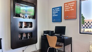 Ein Zimmer mit einem großen Flachbildfernseher an der Wand, einem Schreibtisch mit einem Computer und einem Sessel. An der Wand hängen zwei motivierende Plakate.