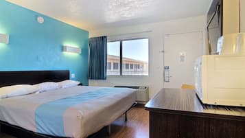 A hotel room with a bed, a desk, a microwave, a window with curtains, and a door.
