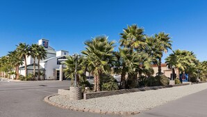 A hotel with a parking lot, palm trees, and a clear blue sky. - Motel 6 Beatty, NV - Death Valley (Beatty)