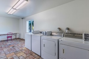 A laundry room with three washing machines, a chair, and a window.