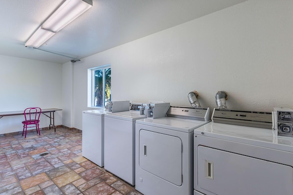 A laundry room with three washing machines, a chair, and a window. - Motel 6 Beatty, NV - Death Valley (Beatty)