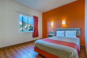 A hotel room with a large bed, a nightstand, a window with curtains, and two wall-mounted lights. - Motel 6 Beatty, NV - Death Valley (Beatty)