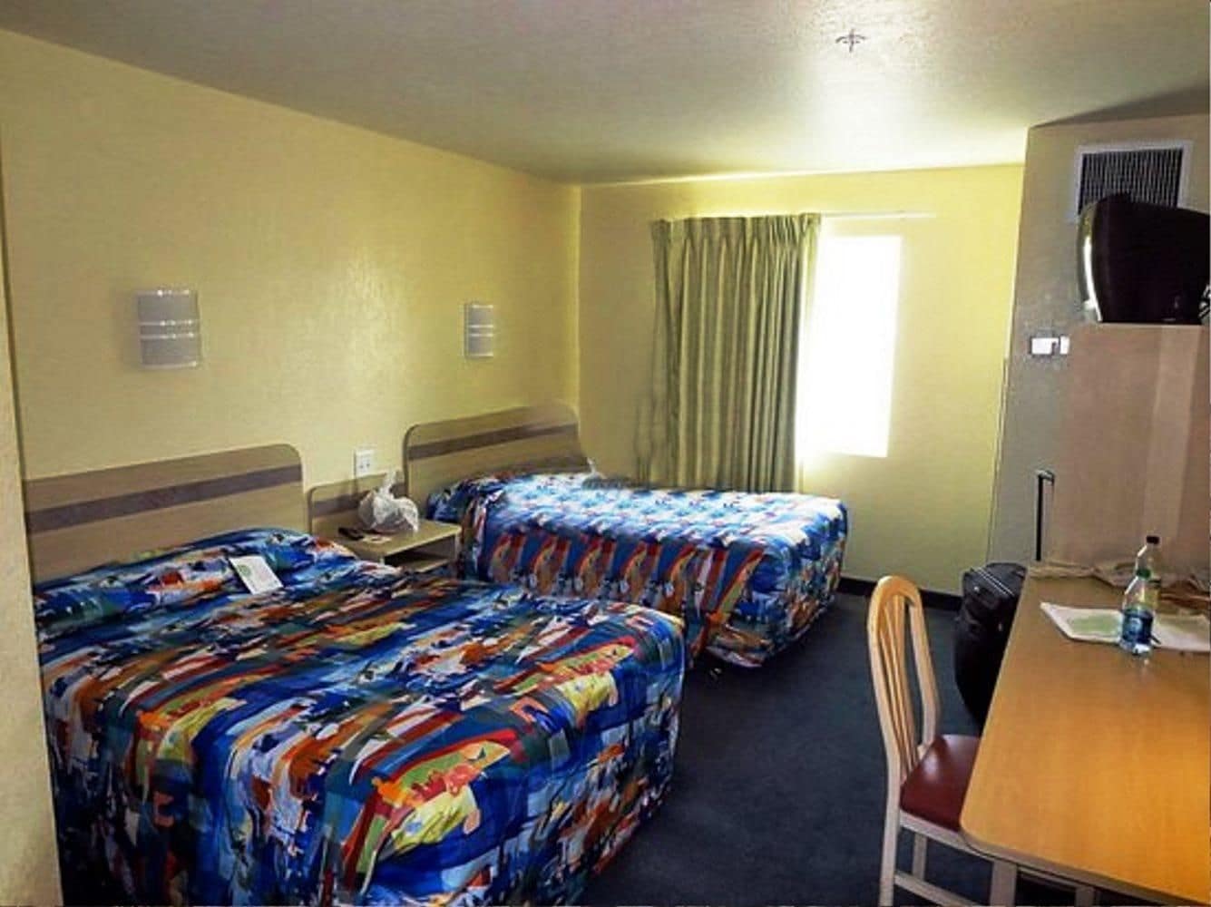 A hotel room with two beds, a desk, a chair, a television, and a window with curtains.