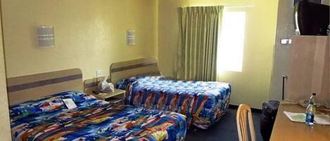 A hotel room with two beds, a desk, a chair, a television, and a window with curtains.