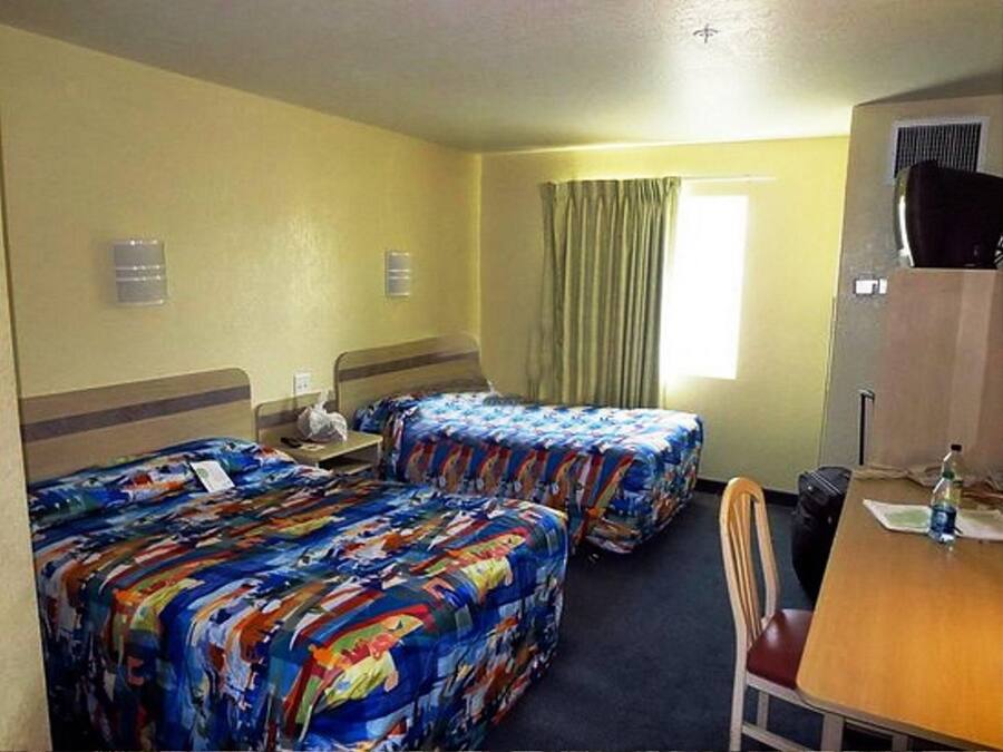A hotel room with two beds, a desk, a chair, a television, and a window with curtains.