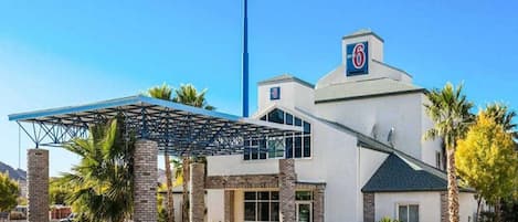 Un hôtel moderne doté d’une entrée couverte, d’un grand panneau indiquant le chiffre « 6 » et d’un parking.