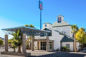 Un hotel moderno con entrada cubierta, un llamativo letrero con el número '6' y un estacionamiento.