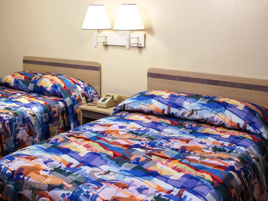 A hotel room with two beds, each with a colorful quilt, a bedside table with a lamp, and a telephone.