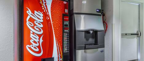 Ein Coca-Cola Getränkeautomat und ein Edelstahlkühlschrank in einem Flur.