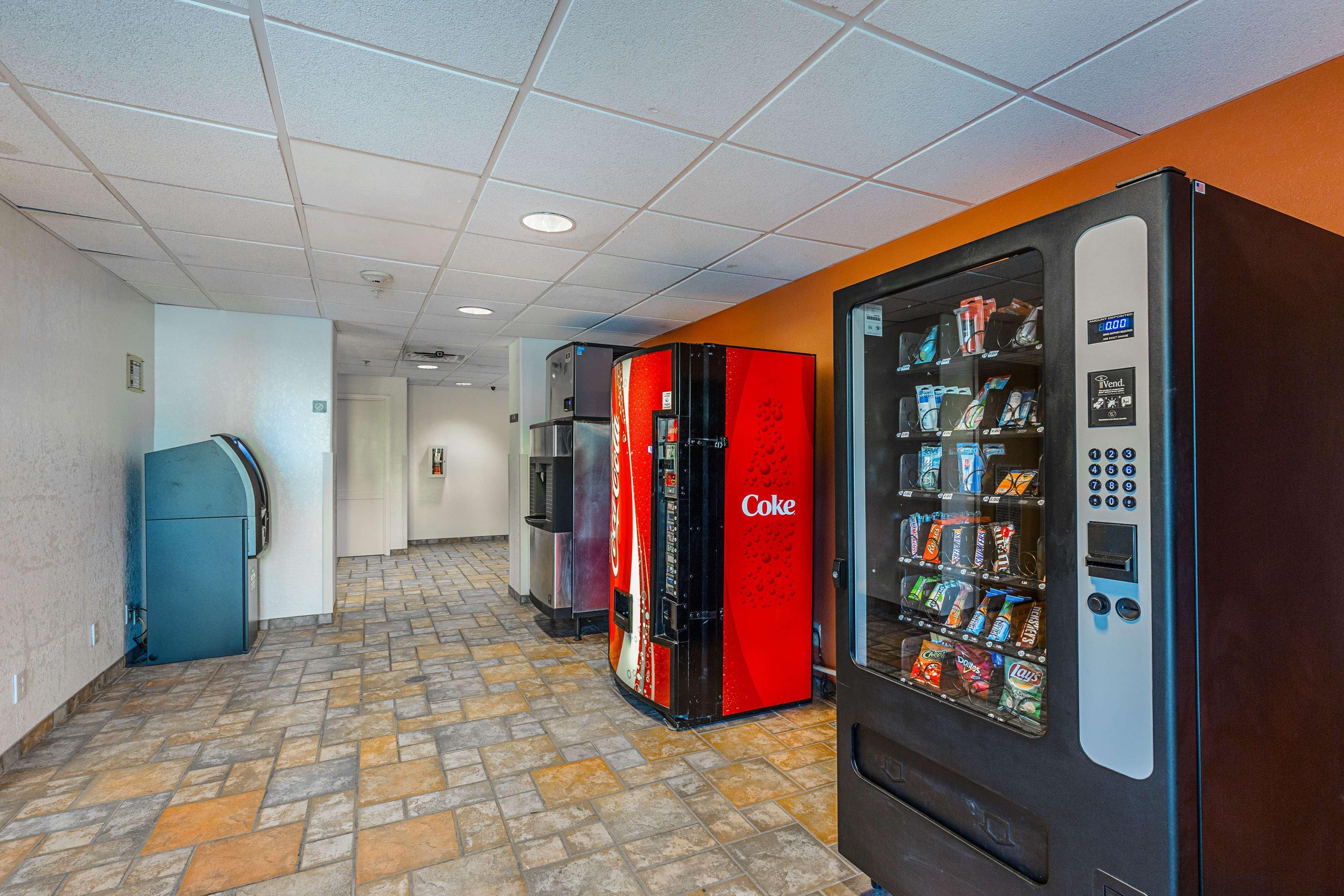 A corridor with vending machines, a refrigerator, and a Coca-Cola branded refrigerator.