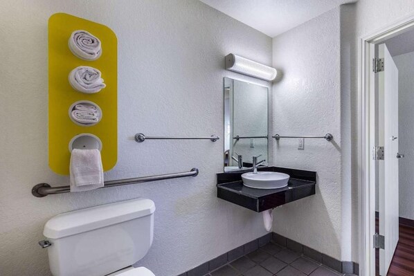 Une salle de bain comprenant des toilettes, un lavabo, un miroir, un porte-serviettes avec des serviettes et une barre d’appui.