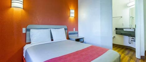 A hotel room with a bed, bedside tables, a mirror, and a bathroom with a sink.