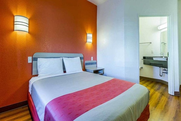 A hotel room with a bed, bedside tables, a mirror, and a bathroom with a sink.
