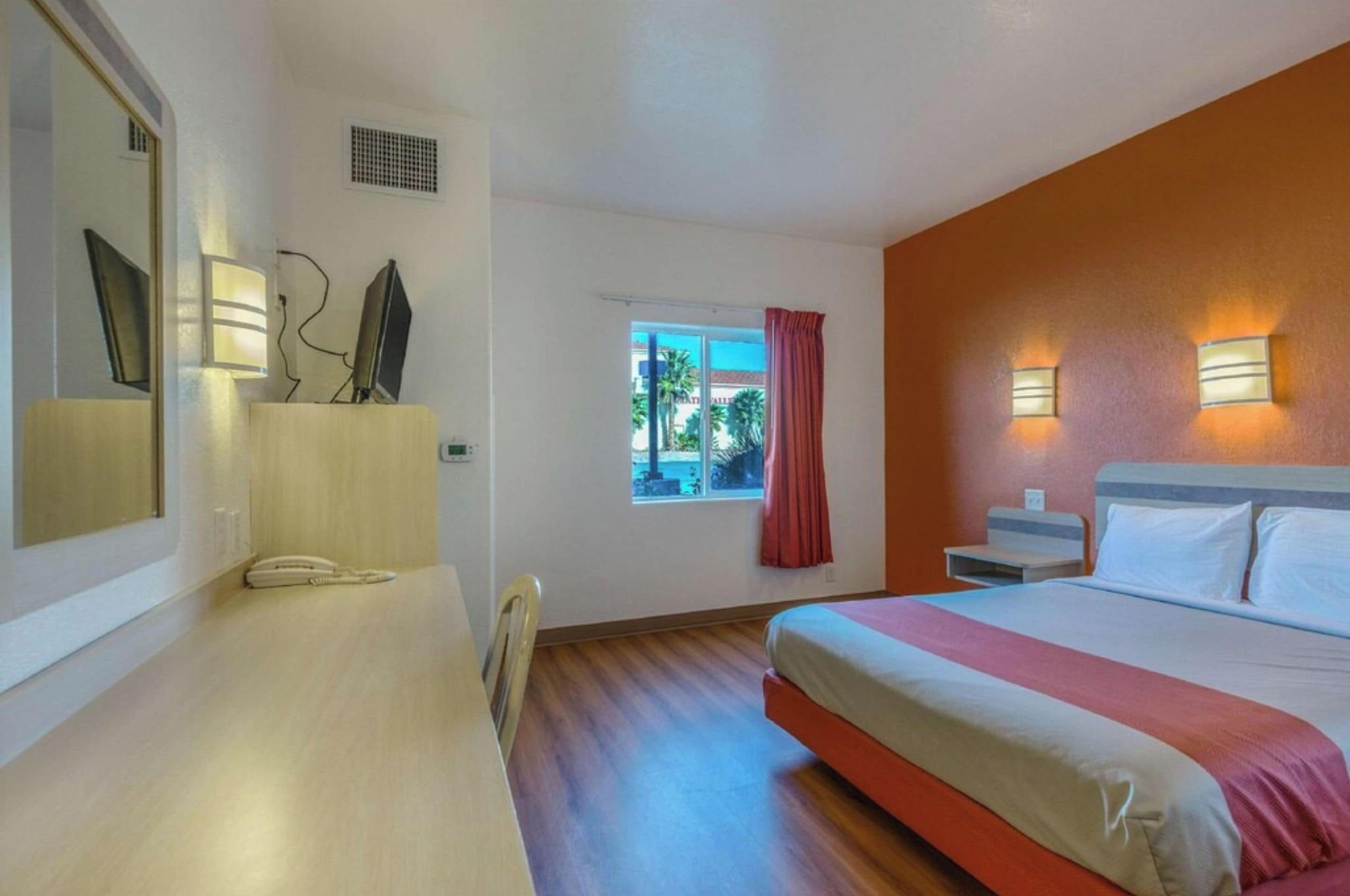 Habitación de hotel con cama, mesita de noche, lámpara, ventana y vistas al exterior.