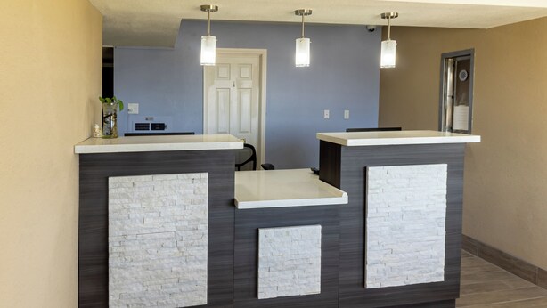 A reception desk with a modern design, featuring a dark wood finish and white stone accents. There are two pendant lights above the desk, and a small vase with a plant on the left side. - Super 8 by Wyndham Big Spring (Big Spring)