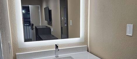 Un baño con un espejo grande, un lavabo blanco y un mueble de tocador oscuro.