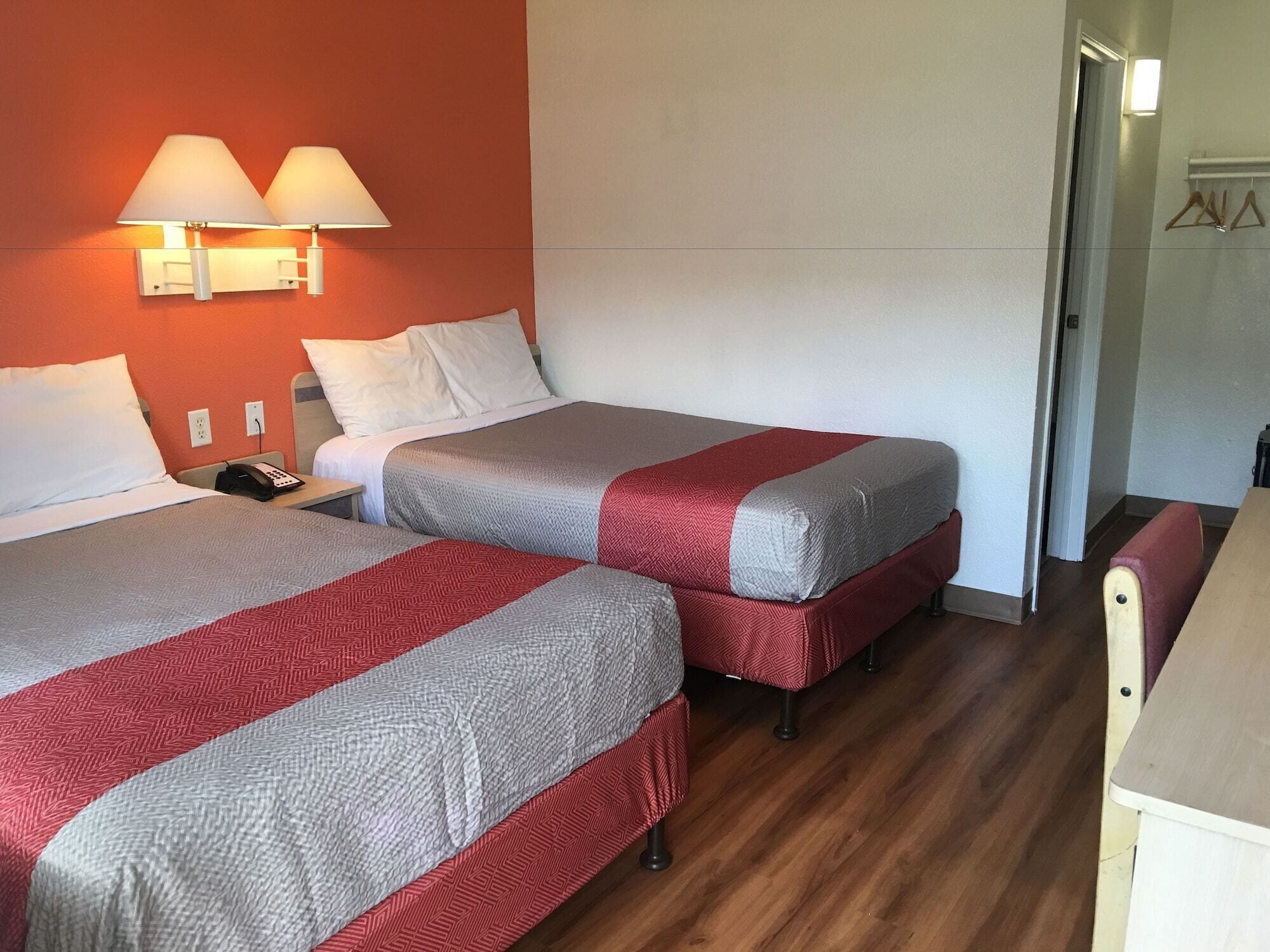 Two single beds with red and grey bedding, a bedside table with a phone, and a wall-mounted lamp.