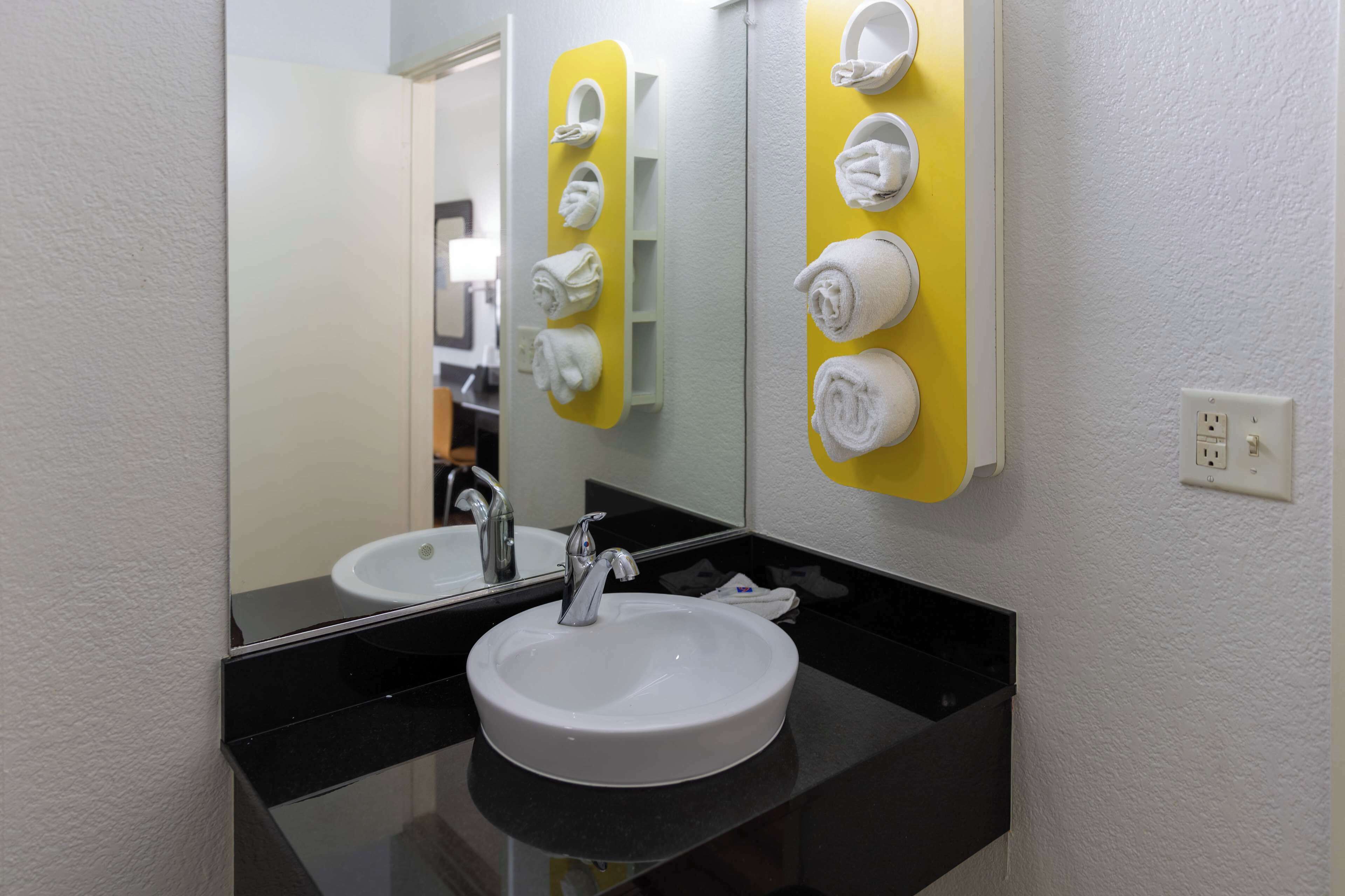 A bathroom with a white sink, black countertop, and a mirror. There are towels hanging on a yellow towel rack.