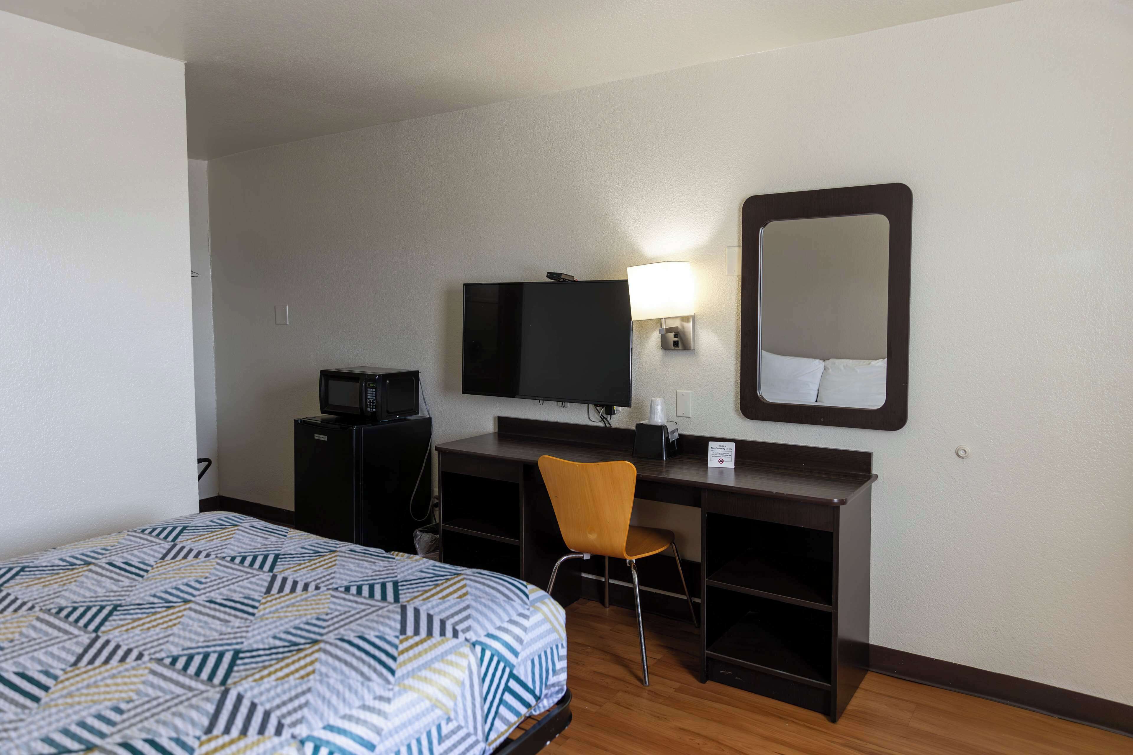 A hotel room with a bed, a desk, a chair, a television, and a mirror.