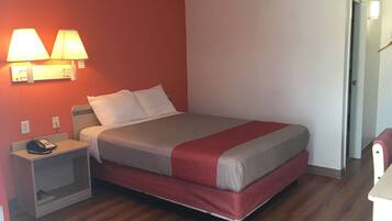 A hotel room with a bed, bedside lamps, a phone on a nightstand, and a door to another room.