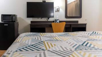 A hotel room with a bed, a desk, a television, a microwave, and a chair.