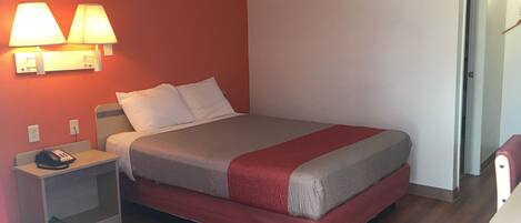 A hotel room with a bed, bedside lamps, a phone on a nightstand, and a door to another room.