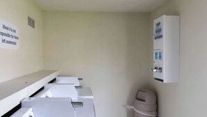 A laundry room with multiple washing machines, a sign indicating the motel is not responsible for unattended items, and a soap and bleach dispenser. - Motel 6 Lufkin, TX (Lufkin)