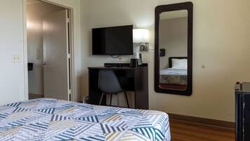 A hotel room with a bed, a desk, a chair, a television, and a mirror.