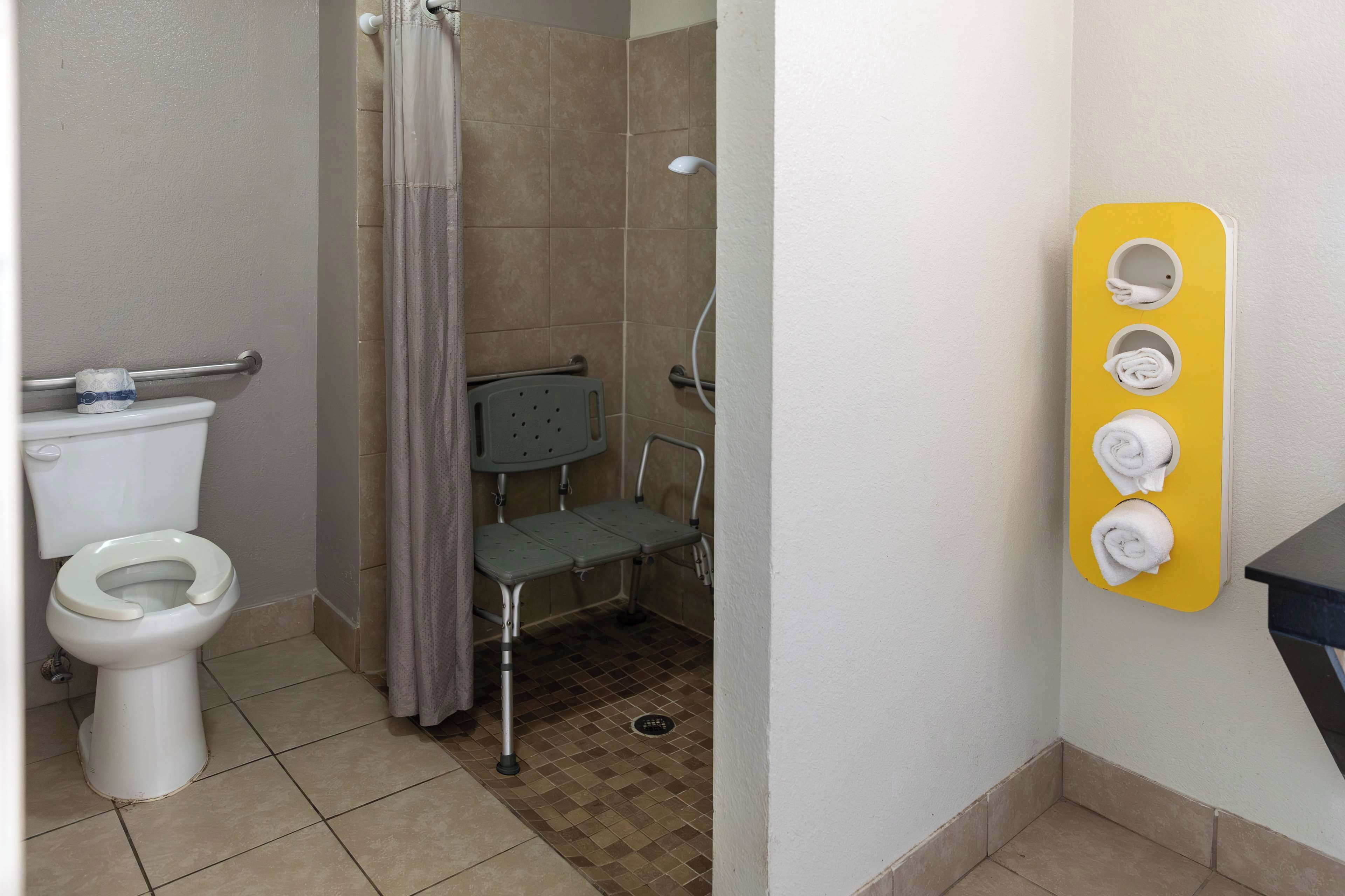 Un baño con inodoro, ducha con barra de apoyo y toallero con toallas.