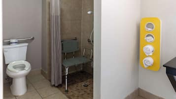 Un baño con inodoro, ducha con barra de apoyo y toallero con toallas.
