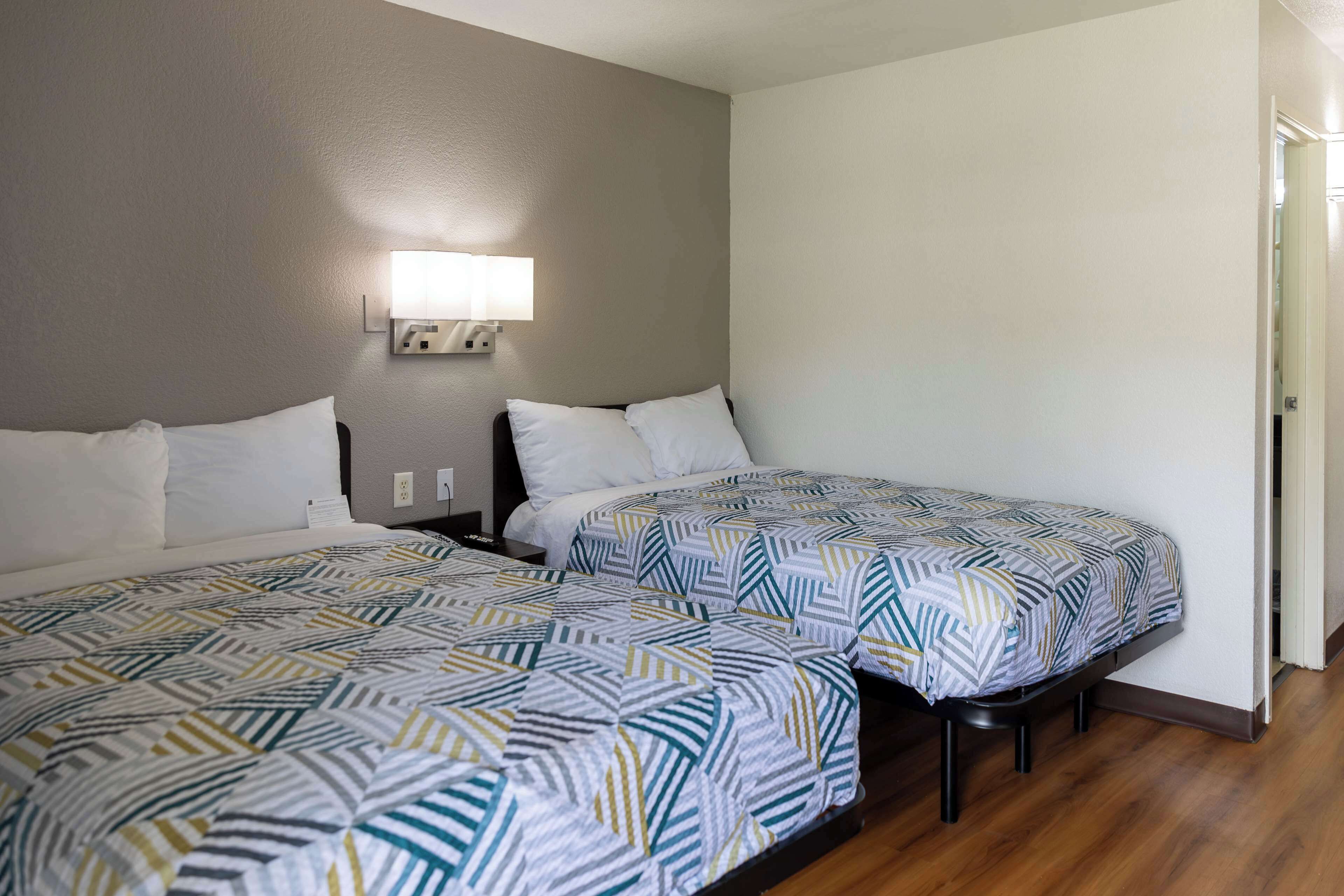 Une chambre d’hôtel avec deux lits simples, une table de chevet, une lampe et une porte sur le côté droit.