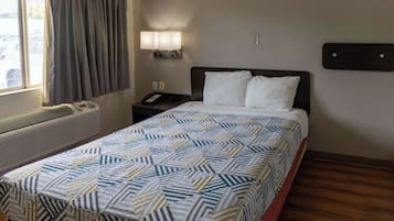 Habitación de hotel con cama, mesita de noche con teléfono, luz de pared y ventana con cortinas.