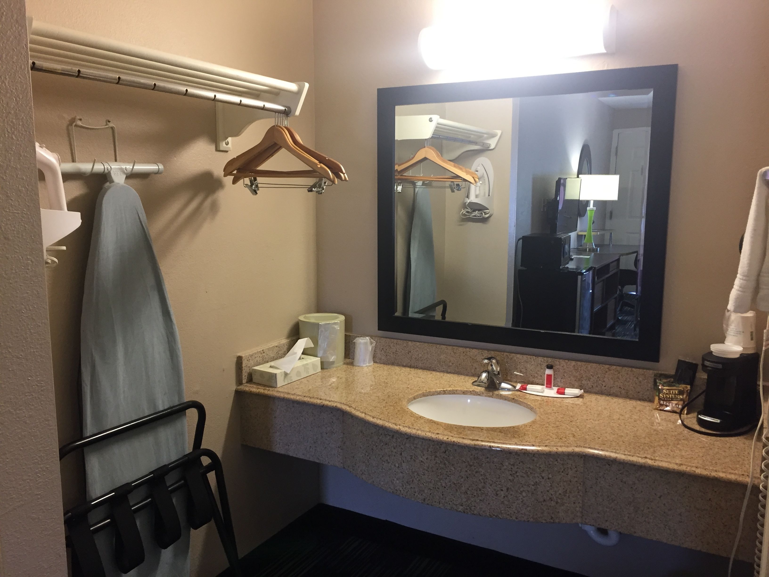 Une salle de bain d’hôtel équipée d’un lavabo en granit, d’un miroir, d’un porte-serviettes, d’une serviette suspendue, d’un distributeur de papier toilette et d’une machine à café.