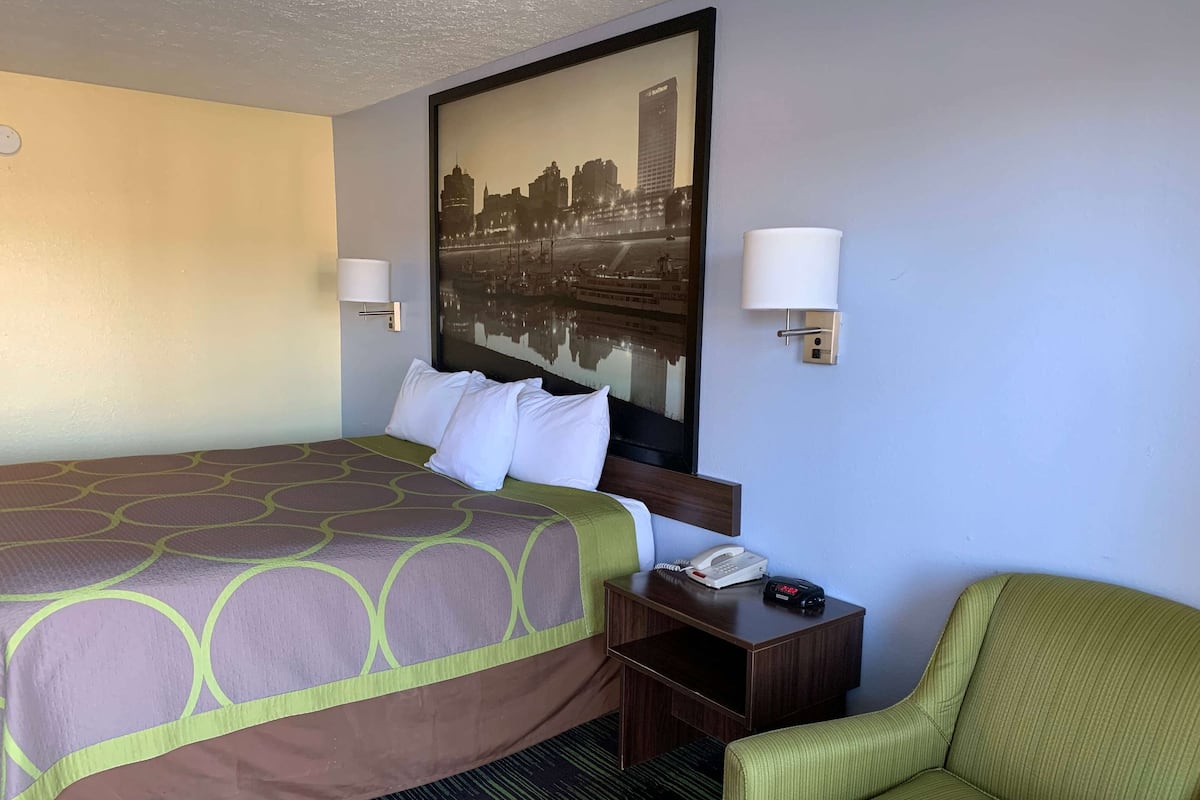 A hotel room with a large bed, two bedside lamps, a nightstand with a phone, and a green armchair.