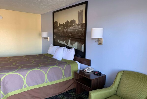 A hotel room with a large bed, two bedside lamps, a nightstand with a phone, and a green armchair. - Super 8 by Wyndham Jackson (Jackson)