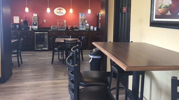 Un restaurante con mostrador de madera, sillas negras y una pared roja con un letrero que dice 'SqueezeStart Breakfast'.
