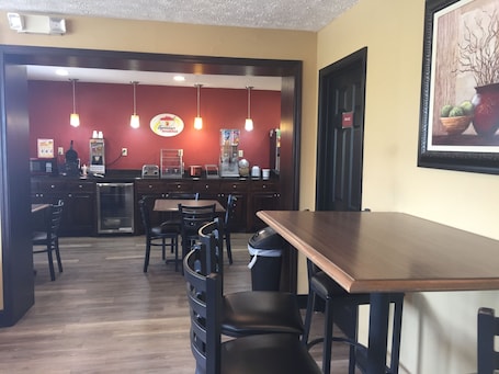 A restaurant with a wooden counter, black chairs, and a red wall with a 'SqueezeStart Breakfast' sign.