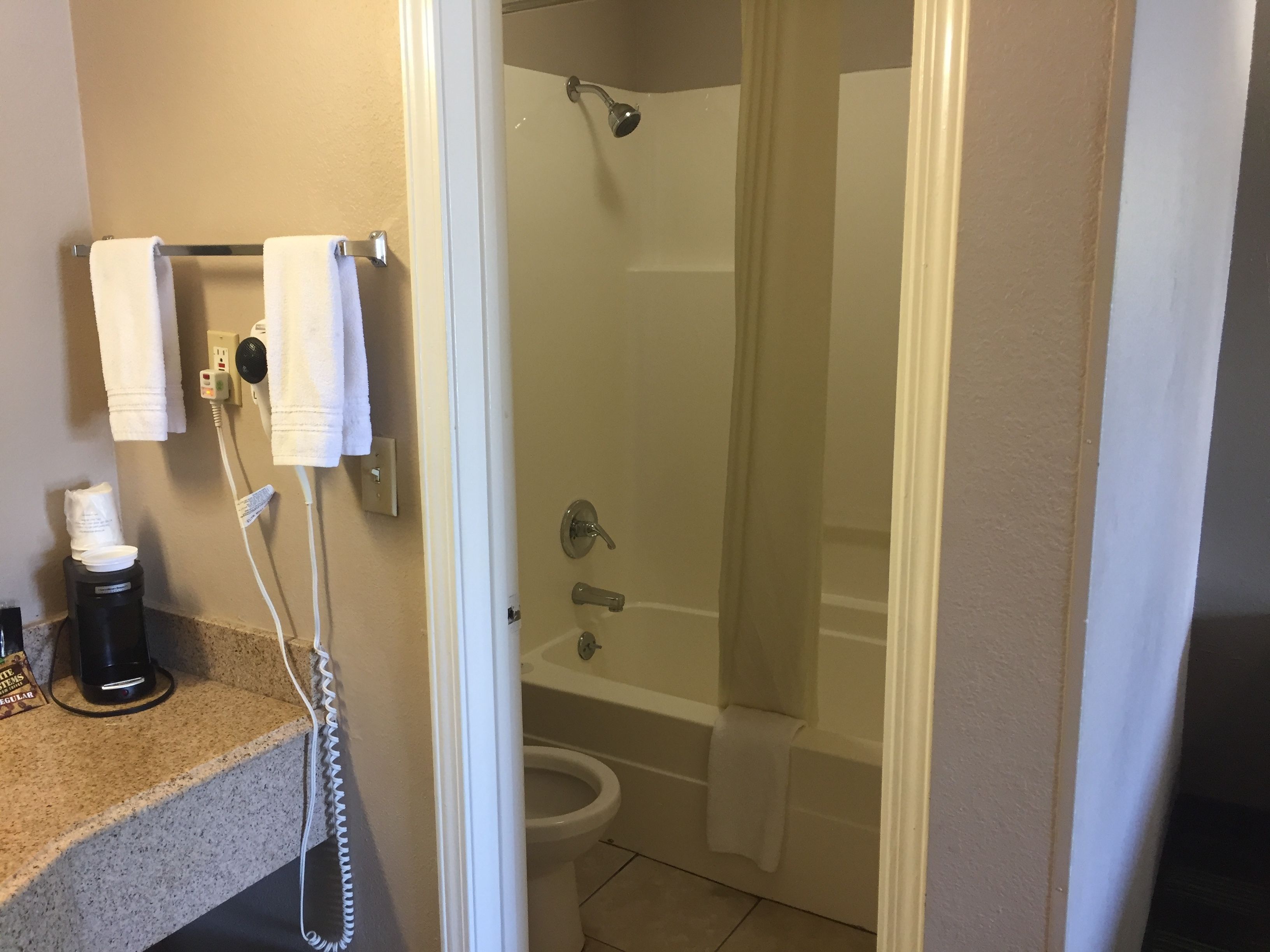 Un bagno con doccia, WC e un piano d'appoggio con una macchina per il caffè e una bottiglia.