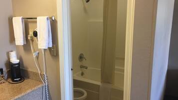 A bathroom with a shower, toilet, and a countertop with a coffee maker and a bottle.