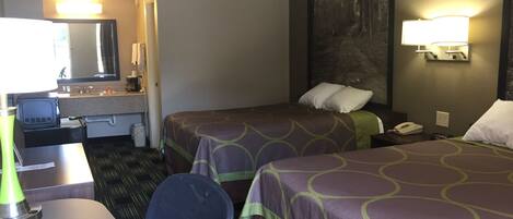 A hotel room with two beds, a desk, a chair, a desk lamp, a telephone, and a wall-mounted light fixture.
