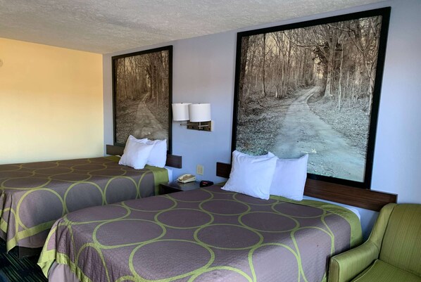 Habitación de hotel con dos camas, una mesita de noche, una lámpara y un cuadro grande con temática de bosque en la pared.