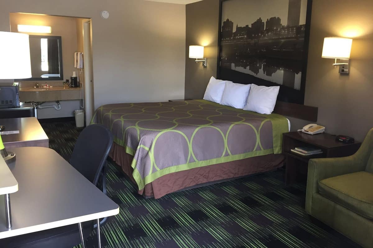 A hotel room with a bed, desk, chair, and a painting on the wall.