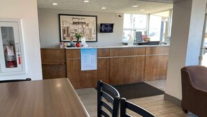 Un área de recepción con mostrador de madera, un extintor, un cartel de bienvenida enmarcado y una pantalla digital.