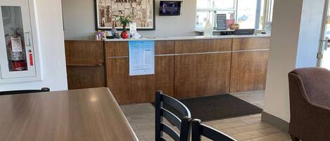 A reception area with a wooden counter, a fire extinguisher, a framed welcome sign, and a digital screen.